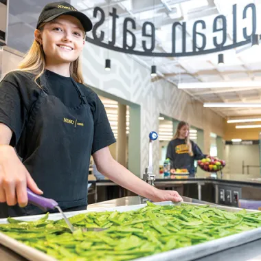 Student worker at Clean eats station scooping peas