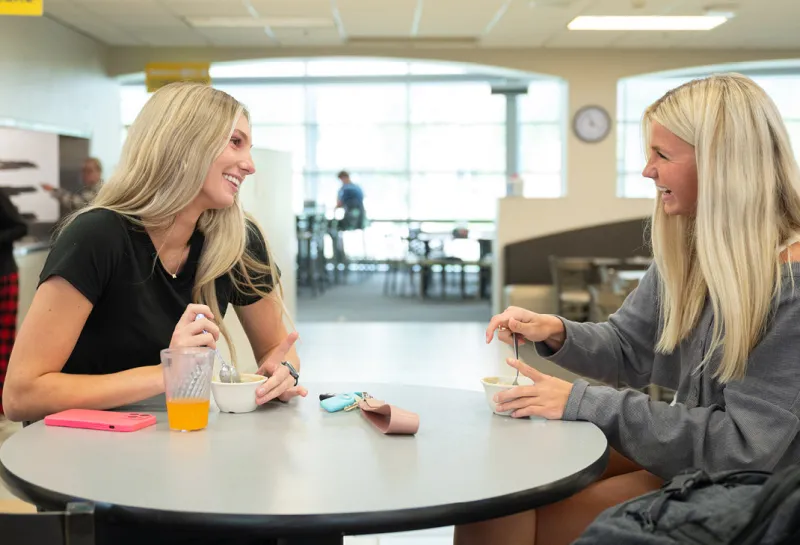 Two women sitting at a table in the Dining Center having a funny conversation