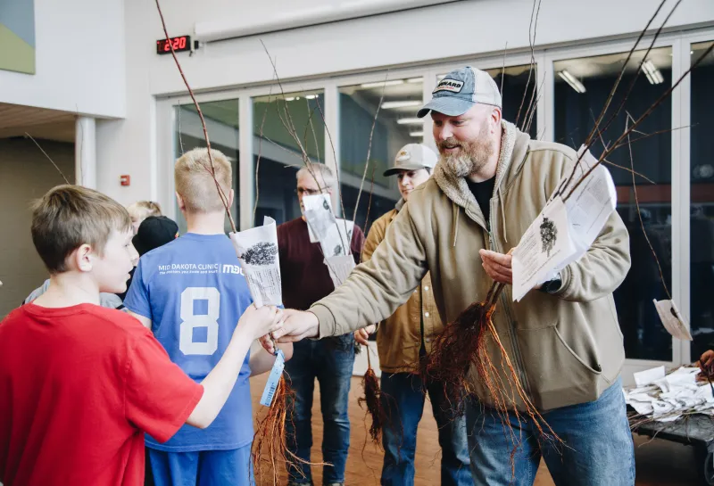 A man with a beard hands a tree seedling to a young boy
