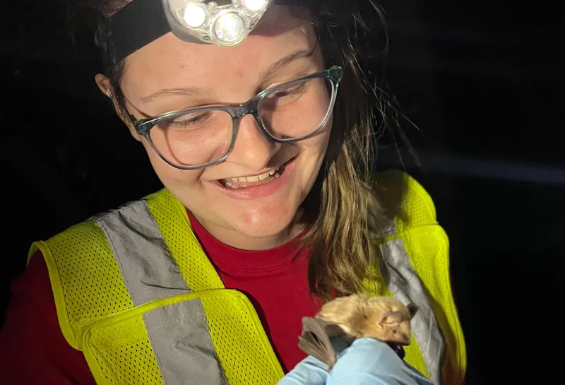 Karliegh wearing gloves, head lamp and yellow vest holding a bat. 
