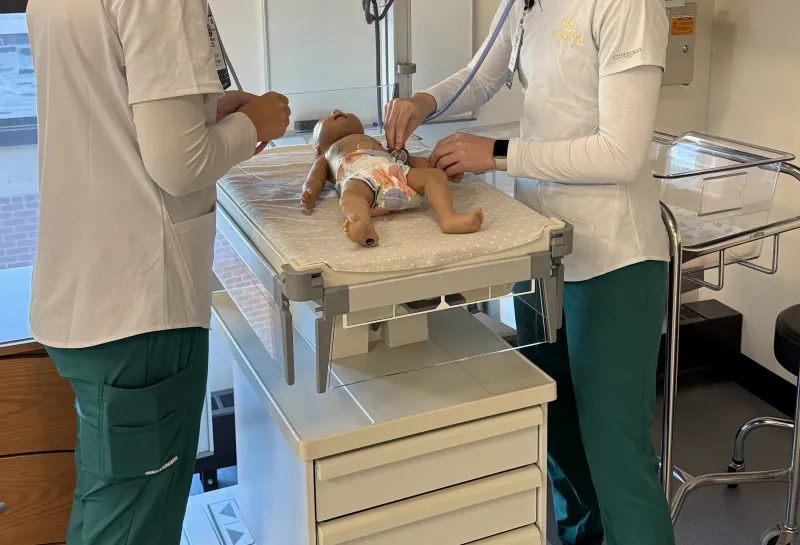 2 nursing students examining sim baby