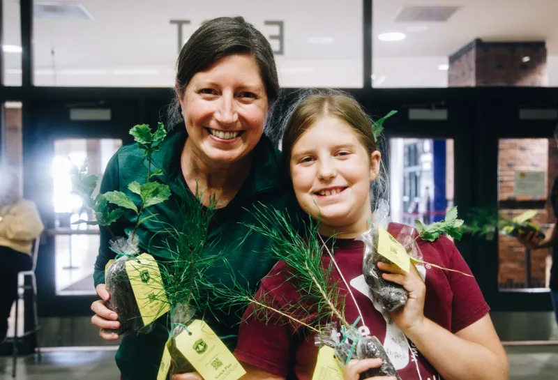 A woman and her daughter smiling while holding tree seedlings