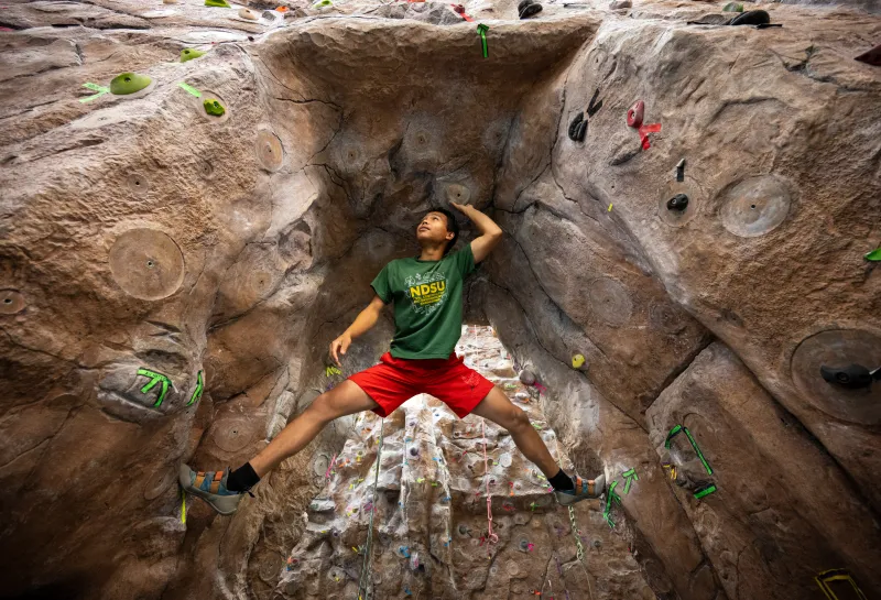 Male student in green shirt in climbing wall niche balancing on side walls