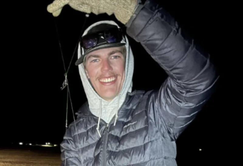 Alec smiling confidently at camera whiled holding a fish.