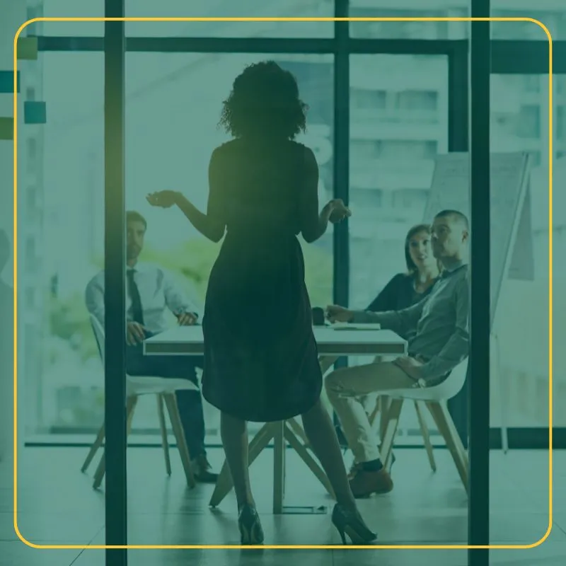 Woman in an office setting presenting to her team of three sitting at a table. 