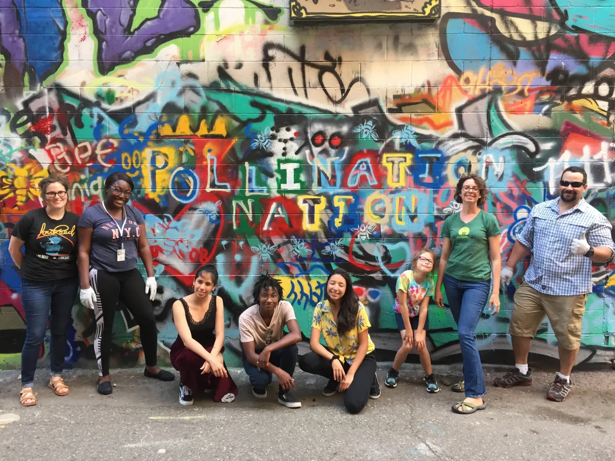 Pollination Nation Students posing in front of a graffiti wall while smiling confidently at the camera.