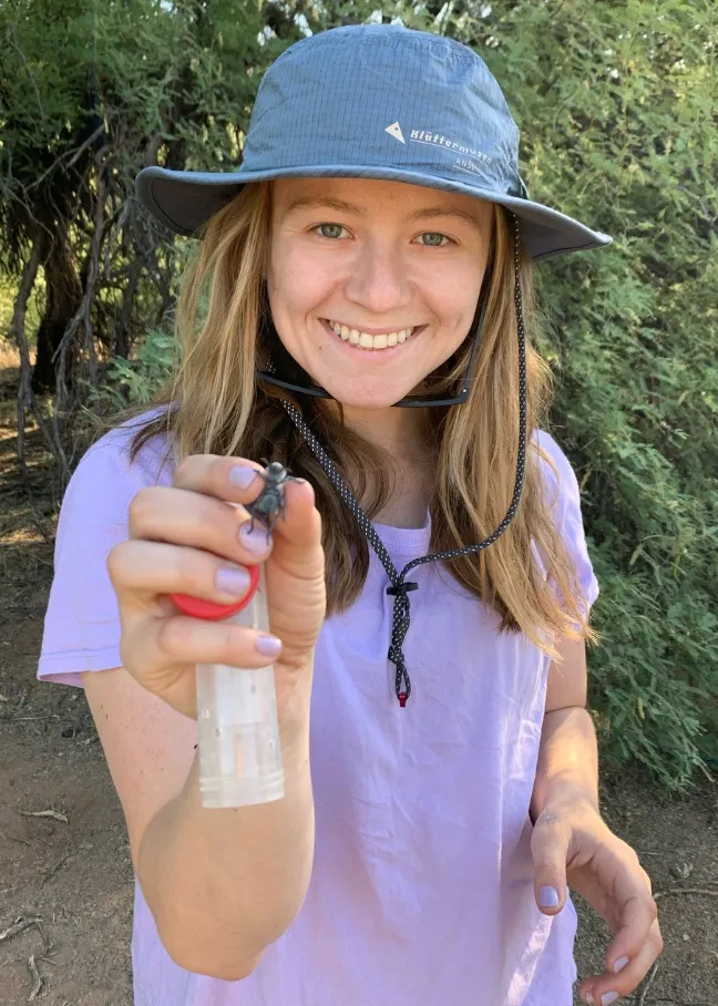 Meredith Johnson holding an insect and lab equipment while smiling confidently at camera.