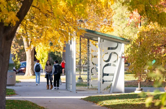 students waiting by bus shelter on campus on a fall day