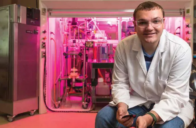 Research Student sitting in a lab smiling confidently at the camera.