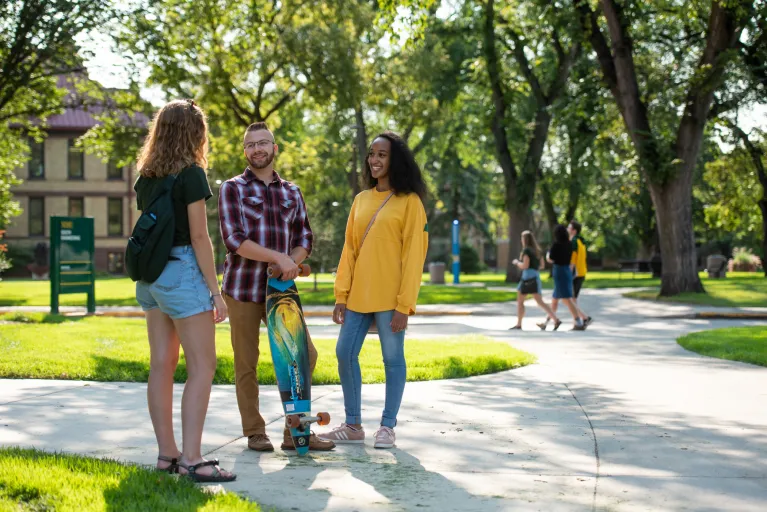 Three students on campus talking on a sunny day.